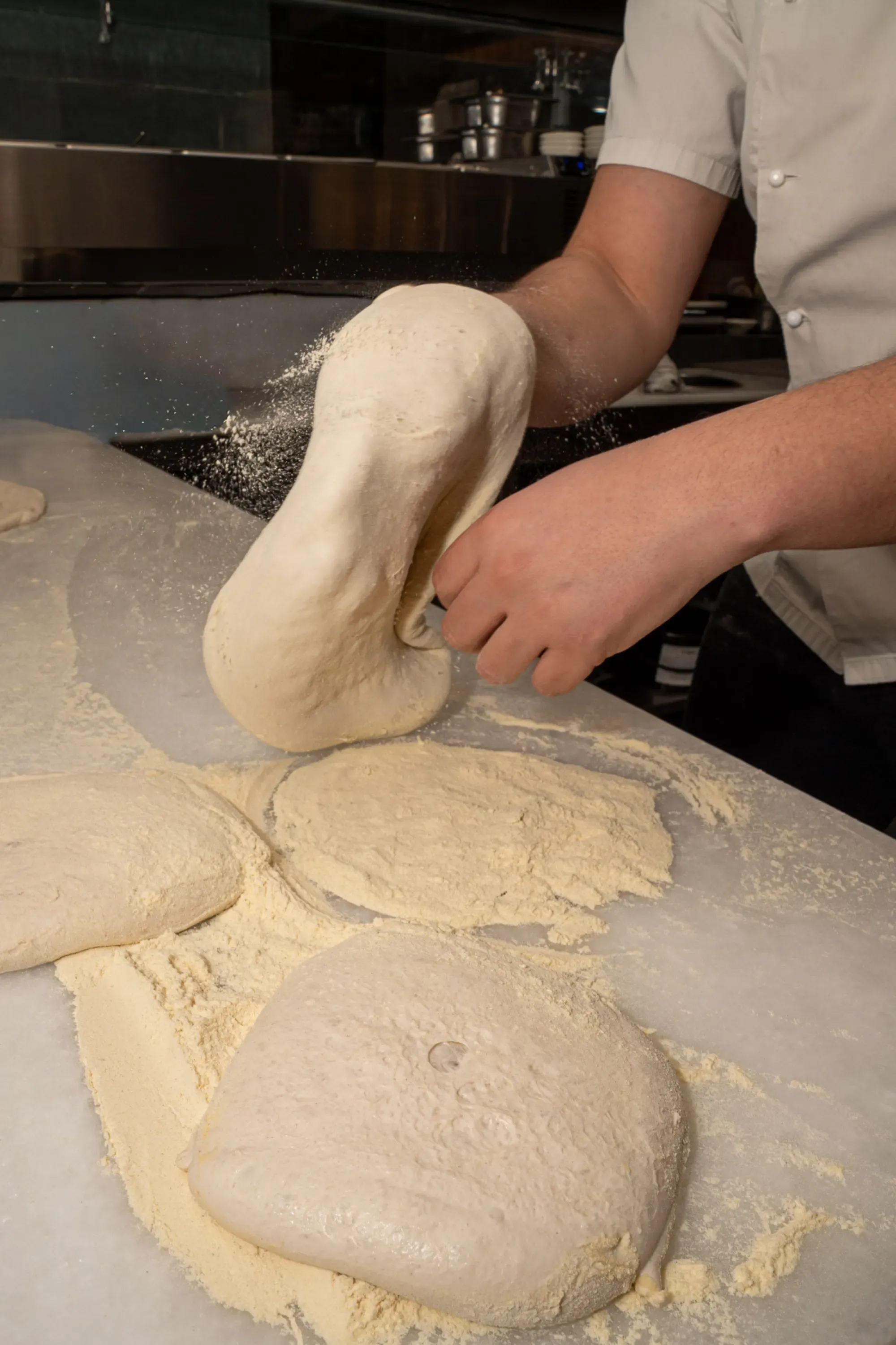 Ο pizzaiolo πλάθει τη ζύμη με αλεύρι στο πάγκο